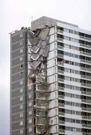 Colour photo of the Ronan Point tower block, post-disaster where one corner has collapsed with ceilings hanging like loose tiles