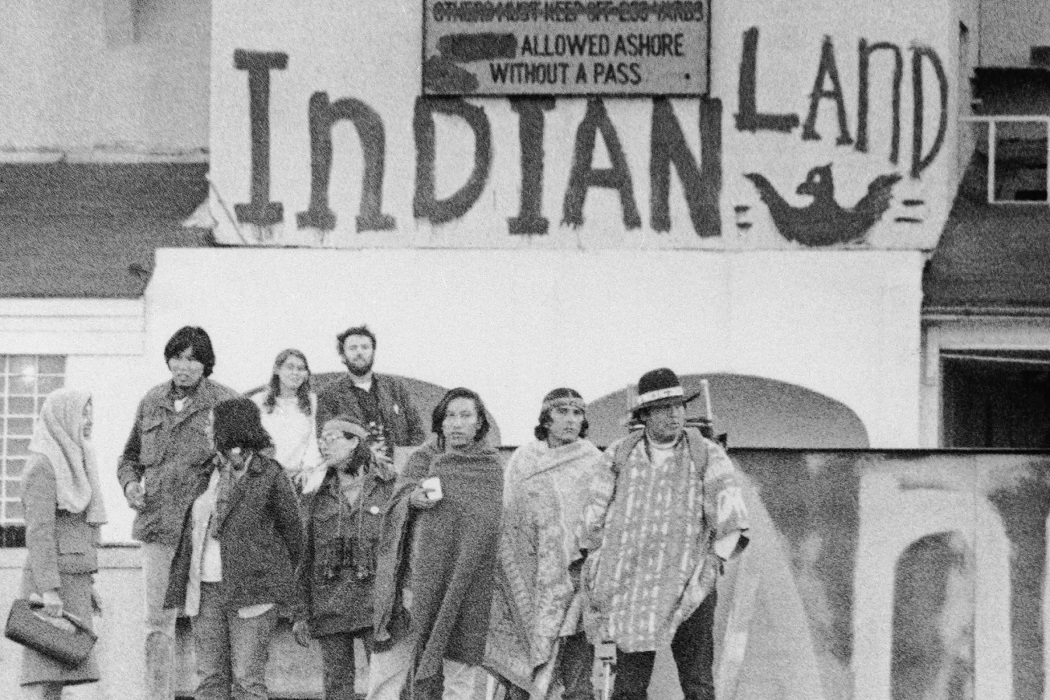 Some of the occupiers a few days after arriving on Alcatraz standing before a painted sign with an eaagle reading 'INDIAN LAND'.