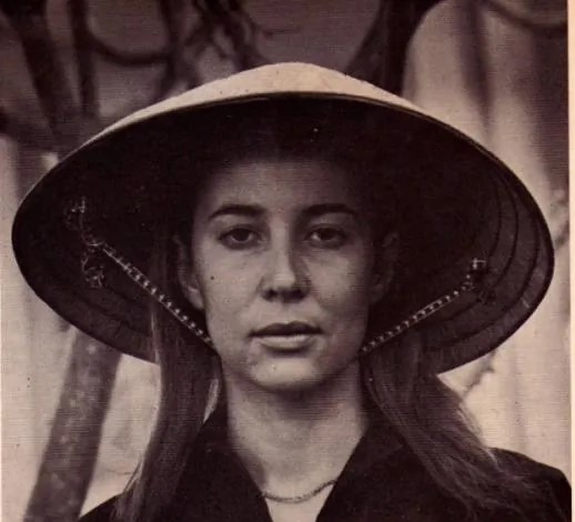 A black and white photo of a young white woman with shoulder length light hair. She is wearing a Vietnamese-style conical hat and is looking at the viewer with a neutral expression.