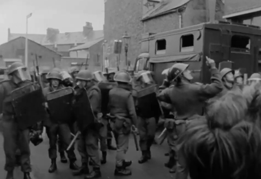 Black and White film still of either police or soldiers, armed with riot gear.