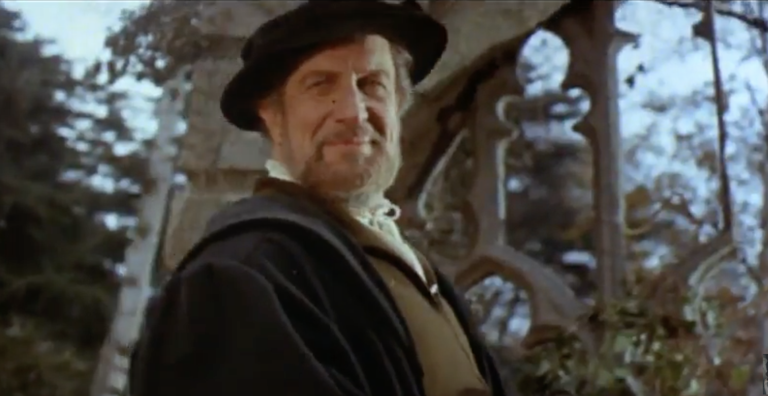 Vincent Price smirking in a ruined church dressed in black seventeenth century clothing