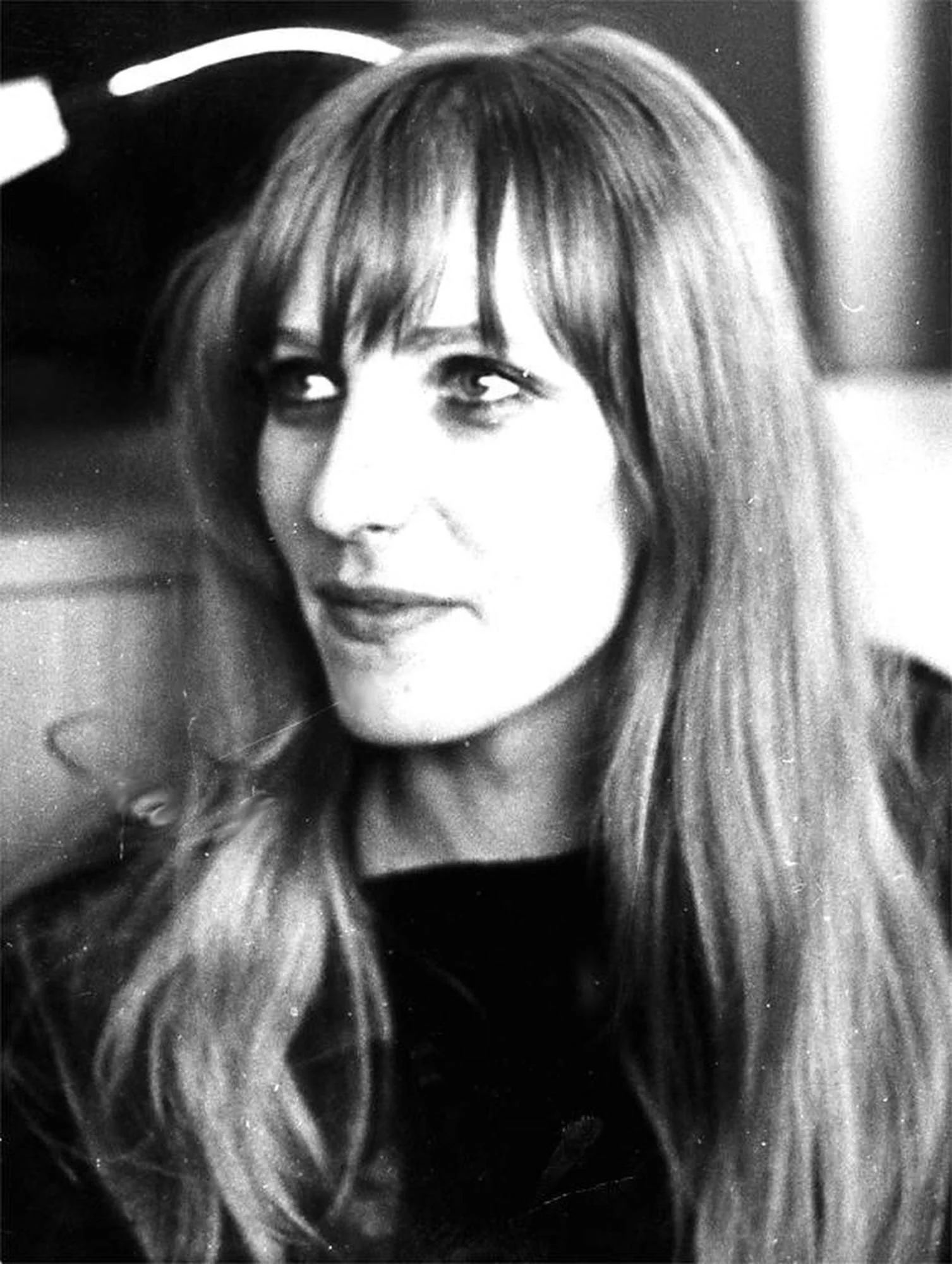 A black and white head shot of Gudrun Ensslin. She wears her hair down in front of her shoulders and has a dark top. She is looking to the left of the viewer with a smile on her face.
