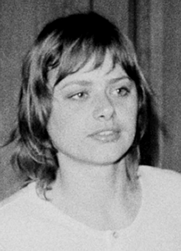 A black and white headshot of a young woman with shaggy short hair and a white t-shirt looking to the right of the viewer.