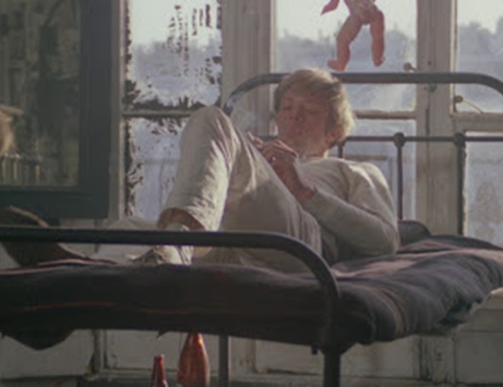 Max lying on his bed in a rundown apartment, looking at his hands