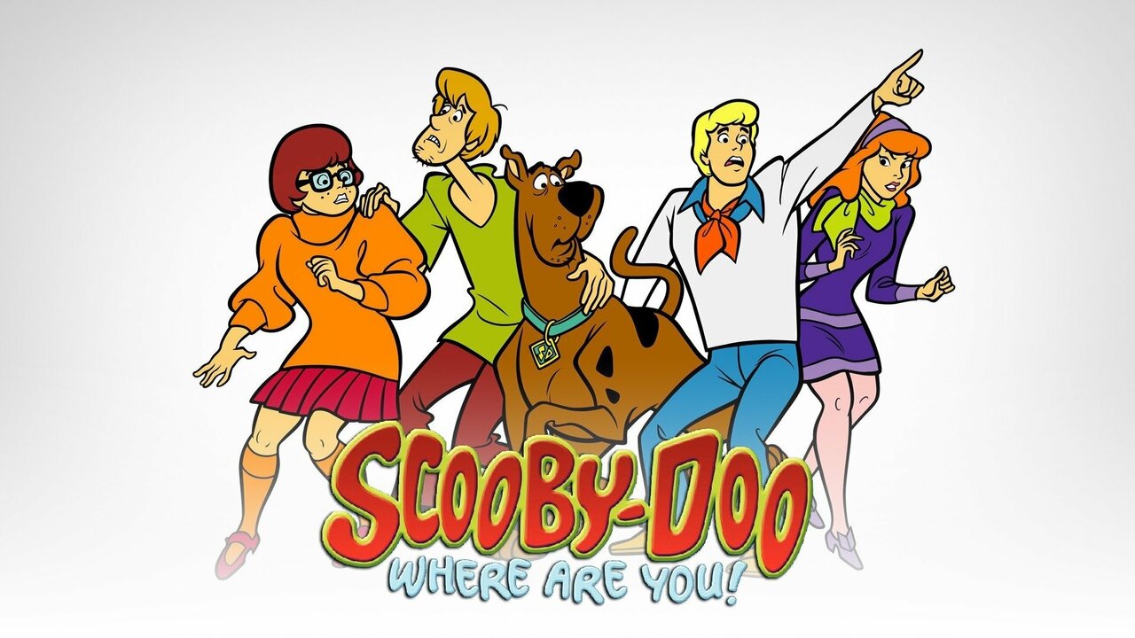 A color image of the cartoon logo for Scooby-doo, Where are you?.  Scooby-Doo is in red capitals with yellow outlines, and Where are you? is in smaller blue capitals.  Behind the title, Velma cringes away from something as Shaggy clutches her shoulder with one hand and Scooby-Doo with the other, his face showing distress.  Scooby also looks alarmed, lifting a front paw and pressing against Shaggy.  Fred points up to the top right of the frame, his face alarmed. Under his arm, Daphne tiptoes forward, her arms held loosely bent in front of her body.